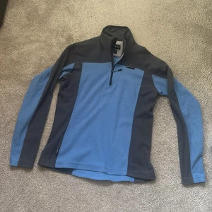 Blå fleece-tröja från Haglöfs - Säljer en blå och mörkgrå fleece-tröja från Haglöfs i storlek 40. Tröjan har lång ärm, hög krage och half zip-dragkedja framtill. Perfekt för kyliga dagar och outdoor-aktiviteter. Mjuk och skön fleece som håller dig varm.