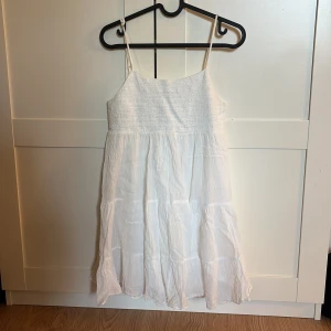 Vit somrig klänning med smala axelband - Luftig vit klänning med smala axelband och rynkad överdel. 