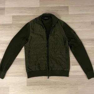 J.Lindeberg Cardigan - Säljder denna feta cardigan/hybridjacka från J.Lindeberg. Den är i väldigt bra skick o har inga defekter. Storlek S. Kommer med kvitto och oginalpåse. Nypris 3000. Skriv vid intresse eller frågor!