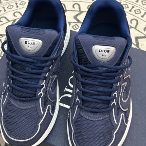 Dior B30 sneakers i marinblå mesh - Säljer ett par Dior B30 sneakers i marinblått med vita och silverfärgade detaljer. Skorna har en sportig design med mesh och syntetmaterial, rund tå, snörning och vit sula. Ikonisk Dior-logga på sidan och på plösen. Perfekta för dig som gillar lyxiga och trendiga sneakers. Skriv i DM vid frågor eller fler bilder🫡🫡