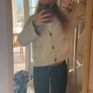 Beige kofta med knappar och fickor - Säljer en beige kofta med stora svarta knappar och två praktiska fickor framtill. Koftan har en avslappnad passform och är stickad i ett mjukt material, perfekt för lager-på-lager. Långärmad och ribbade muddar vid ärmslut och nederkant.