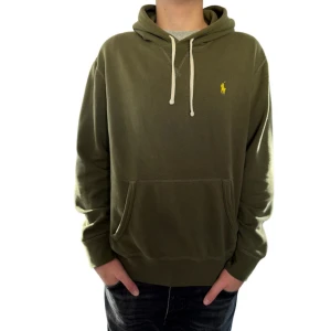 Olivgrön hoodie från Polo Ralph Lauren - Snygg grön hoodie från Polo Ralph Lauren med klassisk gul logga på bröstet. Tröjan har huva med vita snören och en stor magficka framtill. Perfekt för dig som gillar en avslappnad och stilren look.
