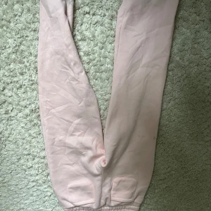 Ljusrosa mjukisbyxor med snörning - Säljer ett par ljusrosa mjukisbyxor med resår och snörning i midjan. Byxorna har två fickor framtill och är tillverkade i mjukt bomullsmaterial. Perfekta för en chill dag hemma eller när du vill vara extra bekväm.