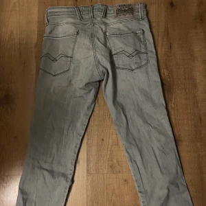 Replay Anbass grå slim jeans - Snygga grå jeans från Replay, modell Anbass med slim fit. Klassisk femficksdesign, svarta detaljer och diskret logga på bakfickan. Jeansen har en smal passform och är tillverkade i mjukt denimtyg som sitter skönt hela dagen.