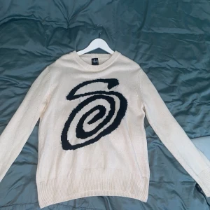 Beige stickad tröja med svart swirl - Säljer en beige stickad tröja från Stussy med swirl på framsidan. Tröjan har rund halsringning och långa ärmar. Perfekt för dig som gillar streetwear och vill ha en skön, lite loose fit. Det enda som är ”dåligt” är att storlekstaggen har åkt av. Sen är den använd men har inte några hål eller något. Pris kan diskuteras