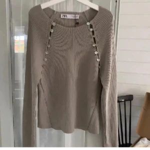 Beige stickad tröja från Zara - Säljer en beige stickad tröja från Zara med snygga knapprader framtill. Tröjan har långärmad design och ribbad struktur som ger en trendig look. 