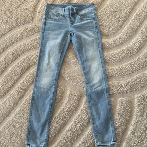 G-Star Raw ljusblå skinny jeans W27 L32 - Säljer ett par ljusblå skinny jeans från G-Star Raw, modell Lynn Mid Skinny. Jeansen har klassisk femficksdesign, med RAW-detalj på fickan och snygga slitningar framtill. Midwaist och stretchigt jeansmaterial för skön passform.
