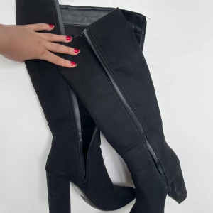 Svarta höga stövlar med klack - Säljer ett par svarta höga stövlar med hög klack och spetsig tå. Skorna har dragkedja längs sidan och är gjorda i mockaliknande material. Perfekta för dig som vill ha en edgy och stilren look.  Köpta för 890kr