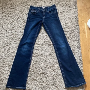 Blå bootcut jeans från Gina Tricot - Mörkblå jeans från Gina Tricot i bootcut-modell med kontrastsömmar och snygga fickdetaljer med lock och knapp bak. Klassisk femficksdesign och dragkedja framtill. Perfekta för dig som gillar en retroinspirerad look.