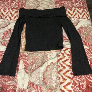 Svart offshoulder topp med utsvängda ärmar - Säljer en svart offshoulder topp med långa ärmar och croppad passform. Toppen har en bred kant upptill som ger en snygg och stilren look. Perfekt att styla med jeans eller kjol för en trendig outfit.