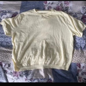 Ljusgul croppad t-shirt - Ljusgul croppad t-shirt med korta ärmar och rund hals. Tröjan har en mjuk och tunn känsla. Resår i nederkant ger en snygg passform. Enkel och stilren design som är lätt att matcha med jeans. En tråd som sticker ut annars ser jag inga fel 