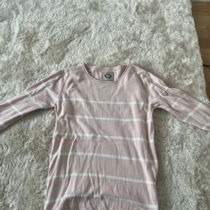 Ljusrosa randig tröja från Etirel XS - Supersöt ljusrosa långärmad tröja från Etirel i storlek XS. Tröjan har vita horisontella ränder och en klassisk rund halsringning. Perfekt för dig som gillar en enkel och stilren look med en touch av pastell.