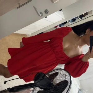 Röd kortklänning med puffärmar - Säljer en röd kortklänning med långa puffärmar och djup fyrkantig urringning. Klänningen har en markerad midja med lätt rynkning och är tillverkad i ett mjukt, flowy material som ger en snygg siluett. Perfekt för dig som vill sticka ut med färg och stil.