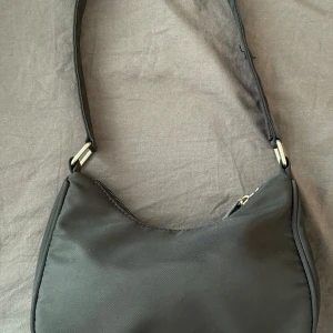 Svart och beige axelväska från Gina Tricot - Två stilrena axelväskor från Gina Tricot, en i svart och en i beige. Båda har minimalistisk design, mjukt syntetmaterial och silverfärgade metalldetaljer. Väskorna har dragkedja upptill och bred axelrem för en trendig look.