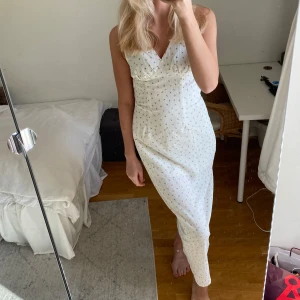 Vit långklänning med småblommigt mönster - Supersöt långklänning i vit nyans med små rosa och grå blommor. Klänningen har v-ringning, är ärmlös och har en figurnära passform. Materialet är lätt och krinklat, perfekt för varma dagar. Dragkedja i sidan för enkel påklädning. Jag på bilden är 175cm och klänningen är i storlek S men skulle säga att den passar S/M. Hör av er vid intresse! ❤️