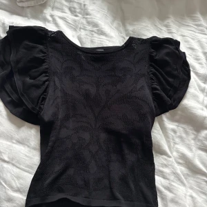 Svart fest topp - Säljer en svart topp med snyggt vävt mönster framtill och puffiga korta ärmar. Toppen har rund halsringning och är figurnära i modellen. Perfekt för dig som gillar unika detaljer och vill sticka ut lite extra. (Den är genomskinlig vid mönsterna!)❤️
