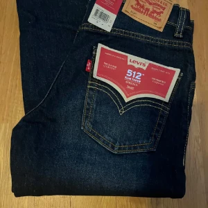Levi's 512 Slim Taper jeans mörkblå - Mörkblå Levi's 512 Slim Taper jeans med snygga kontrastsömmar och klassisk femficksdesign. Jeansen har stretch för extra komfort och en smal, avsmalnande passform. Perfekta för dig som gillar en modern och stilren look.