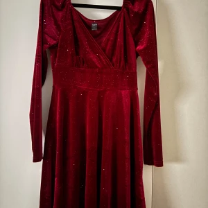 Röd glittrig långklänning från Shein - Säljer en röd långklänning från Shein i storlek S. Klänningen har omlott-ringning, långa ärmar och är gjord i mjuk sammet med glittriga detaljer. Perfekt för dig som vill sticka ut med en elegant och glamorös look.