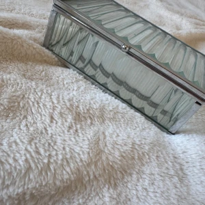 Glas smyckesask med silverkant - Snygg smyckesask i glas med silverfärgad metallram. Asken har ett randigt mönster på både lock och sidor, och insidan är spegelblank. Perfekt för att förvara dina favoritsmycken och ge ditt rum en stilren vibe.