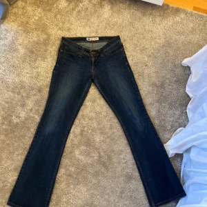 Levi's Demi blå jeans bootcut - Snygga blå Levi's Demi Curve jeans med klassisk femficksdesign och bootcut-ben. Jeansen har mellanblå tvätt, kontrastsömmar och är tillverkade i mjukt denimtyg. Perfekta för dig som gillar en tidlös och avslappnad stil.