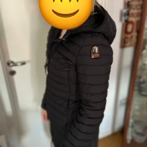 Parajumpers S - Svart, lång och lätt dunjacka från Parajumpers med huva och dragkedja framtill. Jackan har quiltad design, två fickor med dragkedja och klassisk Parajumpers-logga på ärmen. Perfekt för kyliga dagar och riktigt snygg passform. Finns knappt längre att köpa då dom är slutsålda överallt nypris 5700kr