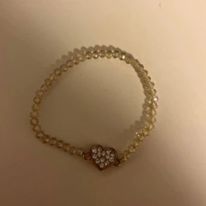 Glittrigt armband med hjärta - Snyggt armband med transparenta pärlor och ett hjärtformat hänge dekorerat med glittrande stenar. Perfekt för dig som gillar söta detaljer och vill ha något som sticker ut lite extra.