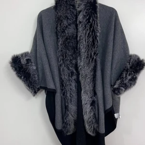 Grå kappa med fuskpälsdetaljer - Snygg grå kappa med breda fuskpälsdetaljer längs krage och ärmslut. Oversized passform och öppen framtill, perfekt för lager på lager. Materialet är mjukt och känns lyxigt, med en mörkare grå insida och fluffig päls-look som ger extra edge.