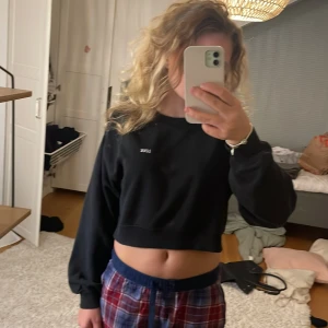 Svart croppad sweatshirt med brodyr - Svart croppad sweatshirt med vit broderad text 'LOVE' på bröstet. Tröjan har långa ärmar och en relaxed fit, perfekt för en chill och trendig look. Mjuk och skön, passar till allt från jeans till mjukisbyxor.