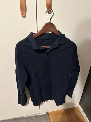 Mörkblå långärmad pikétröja - Snygg mörkblå pikétröja med klassisk krage och långa ärmar. Tröjan är tillverkad i bomull och har en enkel, stilren design utan synliga loggor eller mönster. Perfekt för dig som gillar en clean och chill look. Storlek M. Passar S och är sitter lite kort med L.