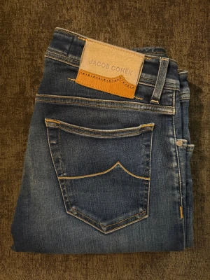 Blå jeans från Jacob Cohën - Snygga blå jeans från Jacob Cohën med klassisk femficksdesign, kontrastsömmar och läderpatch bak i midjan. Jeansen har en stilren look med diskret broderad J på myntfickan och är tillverkade i mjukt denimtyg för en bekväm känsla.