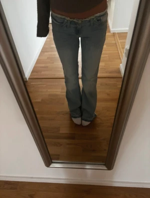 Ljusblå bootcut jeans låg midja - Säljer ett par ljusblå jeans med låg midja och bootcut passform. Jeansen har klassisk femficksdesign, dragkedja och knapp framtill. Perfekta för dig som gillar en avslappnad och trendig look med 00-talsvibbar.