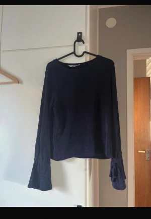 Mörkblå långärmad tröja med knyt - Snygg mörkblå långärmad tröja med knyt vid ärmsluten. Mjuk och skön, perfekt för dig som gillar stilrena plagg med en twist. Passar dig som vill ha något enkelt men ändå lite extra.