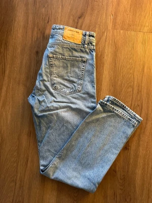 Ljusblå loose fit jeans Jack & Jones - Ljusblå jeans från Jack & Jones i loose fit-modell. Klassisk femficksdesign, raka ben och hög midja. Tillverkade i bomull med knappgylf och snygga kontrastsömmar. Perfekta för en avslappnad och trendig look.