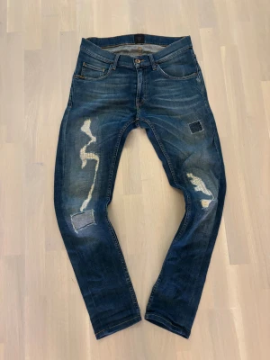 Tiger of Sweden jeans - Snygga blå jeans från T/7 med slitna och patchade detaljer på benen. Modellen har klassisk femficksdesign, smal passform och coola kontrastsömmar. Jeansen är tillverkade i robust denim och har en modern look med lagade hål och unika mönster.