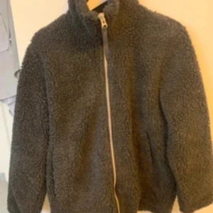 Mörkgrå teddyjacka från Björn Borg - Mysig mörkgrå teddyjacka från Björn Borg i storlek XS. Jackan har hög krage, grov dragkedja framtill och två sidofickor. Materialet är fluffigt fleece som ger en cool och avslappnad vibe. Perfekt för dig som gillar streetstyle och vill hålla dig varm.