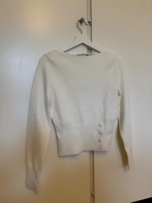 Vit stickad tröja från Bik Bok XS - Vit stickad tröja från Bik Bok med lång ärm och snygga knappar i sidan. Tröjan sitter löst på övre delen och tightare runt midjan, väldigt snygg!! Tröjan är helt ny med prislapp kvar då jag ångrade mig efter köp 🩷