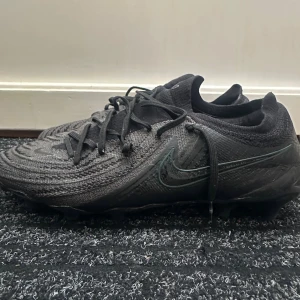 Nike Phantom GX Elite FG – Triple Black - Säljer ett par Nike Phantom GX Elite i helsvart utförande – en av de mest eftertraktade modellerna på marknaden. Lätta, bekväma och med ett supergrepp för max kontroll på planen. Perfekta för dig som vill ha premiumkänsla utan att betala nypris som är nästan 3000. 💬 Skriv om du vill ha fler bilder!