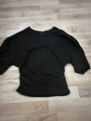 Svart topp från Gina Tricot - En svart, enkel topp från Gina Tricot i storlek S. Modellen har rund hals och korta ärmar, med en klassisk och stilren look. Materialet känns mjukt och stretchigt, perfekt för en chill och clean outfit. Passar dig som gillar basic och minimalistisk stil. Tajt tröja runt midjan 