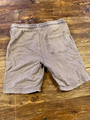 Grå shorts med snörning från Lyle & Scott (mjukis shorts) - Säljer ett par grå shorts från Lyle & Scott med elastisk midja och snörning framtill. De har två stora fickor fram och en bakficka, samt den klassiska gula Lyle & Scott-loggan på ena sidan.