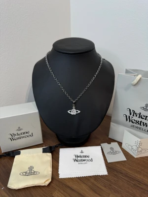 Vivienne Westwood halsband med glittrig orb - Snyggt halsband från Vivienne Westwood i silverfärgad metall med ikonisk orb-berlock dekorerad med glittrande stenar. Kedjan har en klassisk karbinlås och en liten tag med loggan. Levereras med originalförpackning, tygpåse och putsduk.