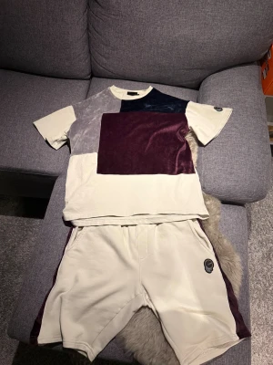 Patchwork set från La Vichy S - Unik t-shirt från La Vichy i storlek S med cool patchwork-design. Färgerna är beige, vinröd, grå och mörkblå, med stora sammetsrutor på framsidan. T-shirten har korta ärmar och rund hals. Materialmix med både bomull och sammet för extra skön känsla.