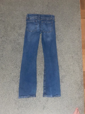 Blå bootcut jeans med låg midja - Snygga blå jeans med bootcut passform och låg midja. Klassisk femficksdesign och lätt slitna detaljer framtill och baktill. Perfekt för dig som gillar en avslappnad och trendig stil. Materialet är jeans med skön stretch. Säljer pga för korta GÅR EJ ATT HITTA I BUTIK LÄNGRE!
