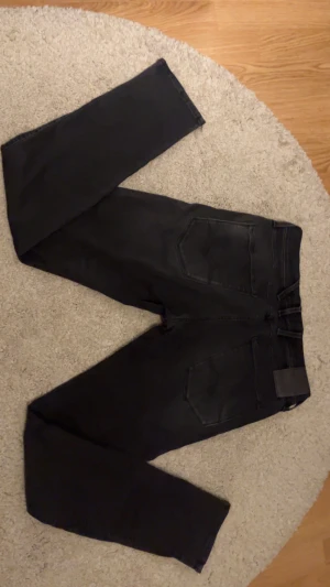 Svarta Replay jeans wide fit - Säljer ett par svarta Replay jeans med klassisk femficksdesign. Jeansen har en mörk tvätt, raka sömmar och logotyp på bakfickan. Passformen är loose och materialet är slitstarkt jeans. Perfekt för dig som gillar avslappnad stil.