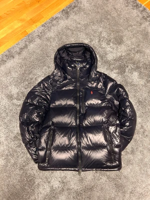 Polo Ralph Lauren - The Gorham Glossed Down Jacket  - SÄLJER: Jacka i nyskick, äkta. Pris 4 600 kr. Nypris 6695 kr. Kvitto och prislapp medföljer.  Köpt 28/11 men passar mig inte. Får endast tillgodo i butik, därför säljer jag. Storlek M, sitter perfekt på mig (182 cm, 75–88 kg). Mycket varm och bekväm, perfekt för vintern och en bra julklapp.  Oanvänd, redo att hämtas eller skickas. Hör av dig!