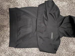 Svart hoodie Peak Performance 160 - Svart hoodie från Peak Performance med klassisk logga på bröstet. Tröjan har huva, stor magficka och ribbade muddar vid ärmslut och nederkant. Materialet är mjuk bomull och polyester, perfekt för chill eller häng med kompisar.