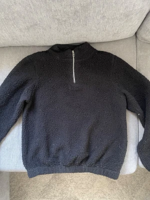 Svart fluffig tröja med half zip - Mysig svart tröja med halv dragkedja framtill och högre krage. Materialet är fluffigt och. Tröjan har långärmad design. Enkel och stilren. Storlek 170 på barnavdelningen. 