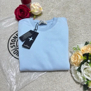 Ljusblå Stone Island sweatshirt - Snygg ljusblå sweatshirt från Stone Island med klassisk rund hals och ribbade muddar. Tröjan har den ikoniska Stone Island-patchen på vänster ärm och är tillverkad i mjuk bomull. Perfekt för dig som gillar stilrena och cleana plagg med streetkänsla.
