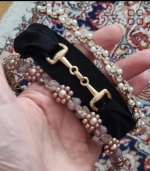 Tre hårband pärlor och gulddetaljer - Säljer tre snygga armband: ett med svart band och guldfärgad hästbetsdetalj, ett med vita pärlor och blommor på guldfärgad stomme, samt ett med ljusrosa pärlor och glittriga stenar i blommönster. Perfekt för dig som gillar unika accessoarer!