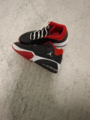 Svarta Nike Jordan sneakers med röd detalj - Snygga Nike Jordan sneakers i svart med röda och vita detaljer. Skorna har en klassisk rund tå, vit snörning och en mjuk röd insida. Ikonisk Jumpman-logga på sidan och en platt sula som ger bra komfort. Perfekt för dig som gillar streetstyle och basketinspirerad look.