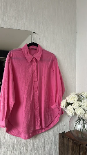 Oversized rosa skjorta med knappar - Snygg oversized skjorta i stark rosa färg med klassisk krage och knäppning framtill. Skjortan har långa ärmar och är tillverkad i ett lätt bomullsmaterial som ger en chill och avslappnad vibe. Perfekt att styla lager på lager eller bära som den är.